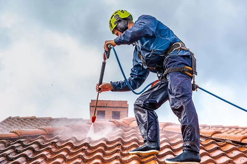 Un homme nettoie à l'aide d'un pulvérisateur à pression la mousse sur un toit